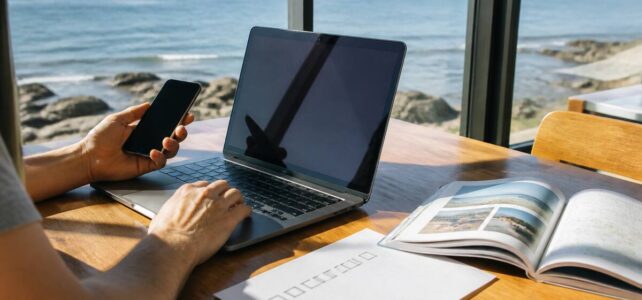 Praktisch vakantieplannen met laptop en reisgids bij een raam met uitzicht op zee